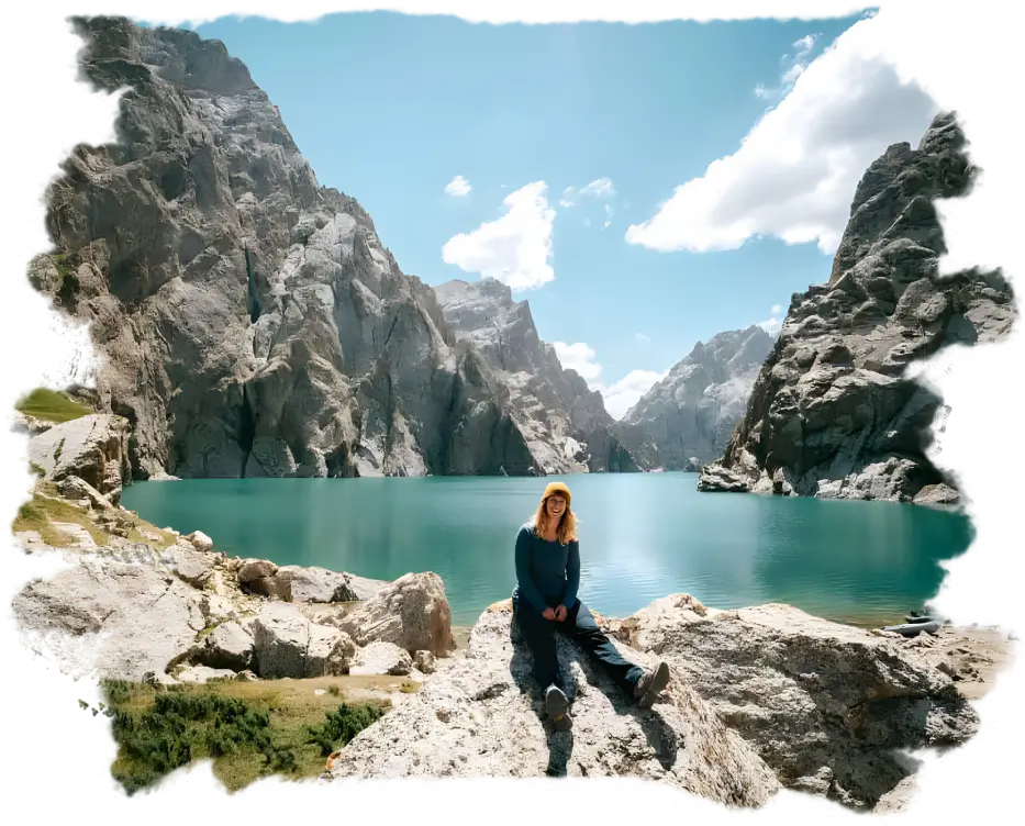 Traveler sitting on rocks at Kel-Suu Lake during Kyrgyzstan Tours, surrounded by dramatic cliffs.